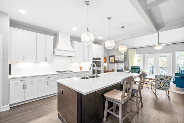 kitchen with custom range hood, a kitchen island with sink, sink, dark hardwood / wood-style floors, and white cabinetry