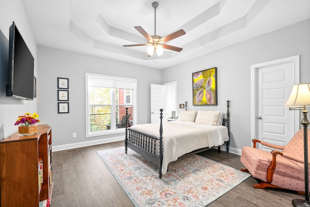 bedroom with a tray ceiling, ceiling fan, and dark hardwood / wood-style floors