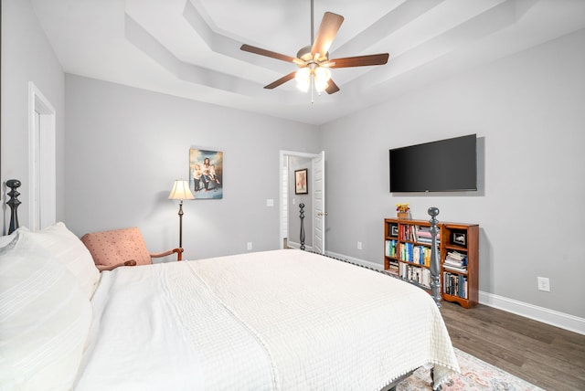 bedroom with a raised ceiling, ceiling fan, and dark hardwood / wood-style flooring