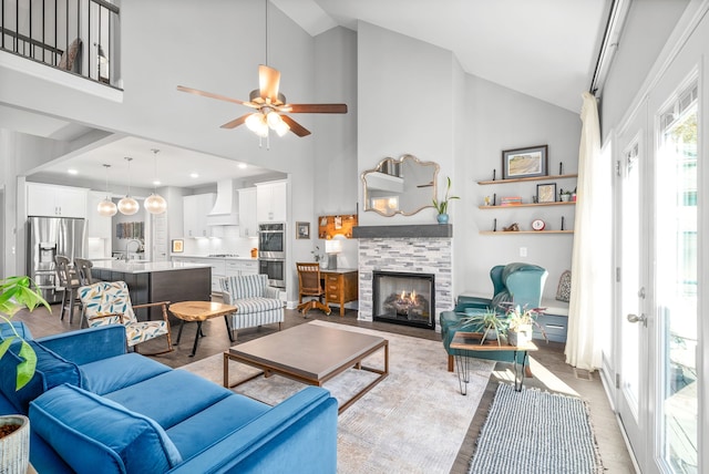 living room featuring light hardwood / wood-style floors, high vaulted ceiling, ceiling fan, and a tiled fireplace