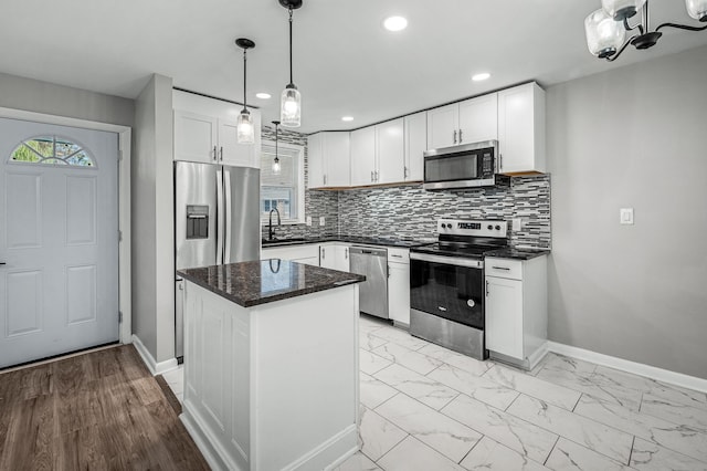 kitchen featuring a center island, backsplash, pendant lighting, white cabinets, and appliances with stainless steel finishes