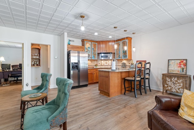 kitchen featuring kitchen peninsula, light stone counters, stainless steel appliances, light hardwood / wood-style flooring, and hanging light fixtures