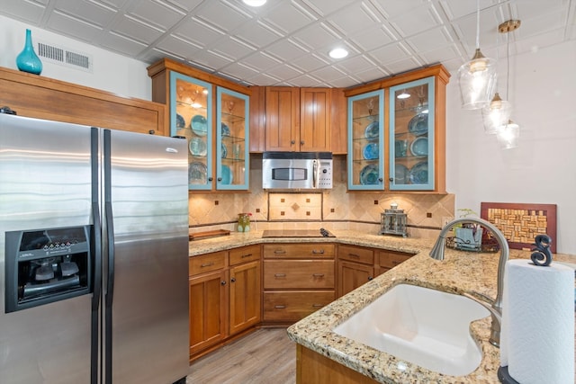 kitchen with light stone countertops, sink, stainless steel appliances, decorative light fixtures, and light wood-type flooring