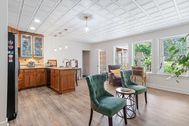 interior space featuring stainless steel fridge, sink, black dishwasher, light hardwood / wood-style floors, and hanging light fixtures