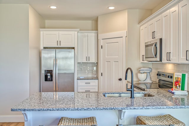 kitchen featuring a breakfast bar area, decorative backsplash, white cabinetry, and appliances with stainless steel finishes