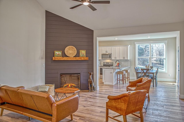 living room featuring lofted ceiling, sink, light hardwood / wood-style flooring, ceiling fan, and a large fireplace