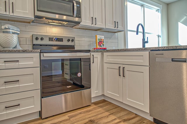 kitchen with stone counters, backsplash, light hardwood / wood-style floors, white cabinets, and appliances with stainless steel finishes