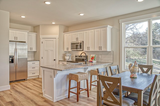 kitchen with kitchen peninsula, appliances with stainless steel finishes, light stone counters, light hardwood / wood-style floors, and white cabinetry