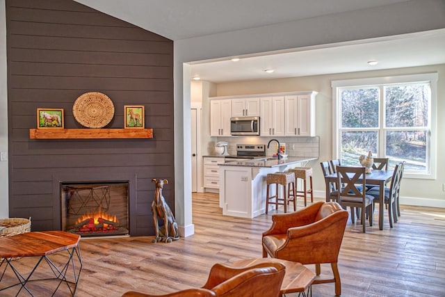 interior space featuring a large fireplace, light hardwood / wood-style flooring, vaulted ceiling, and sink