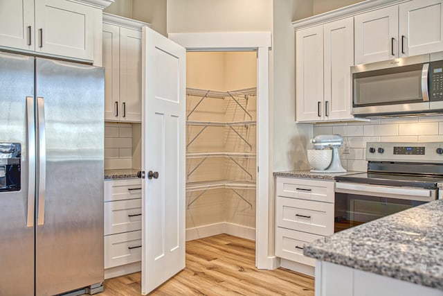 kitchen with light stone countertops, light wood-type flooring, backsplash, stainless steel appliances, and white cabinetry