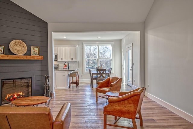 living area with light wood-type flooring, a large fireplace, and vaulted ceiling