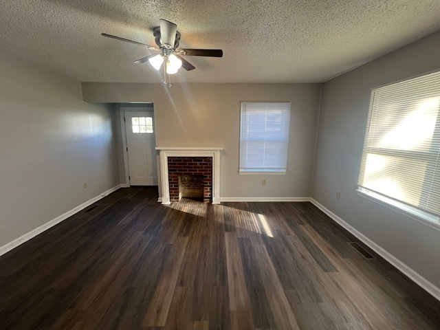 unfurnished living room with ceiling fan, dark wood-type flooring, a textured ceiling, and a brick fireplace