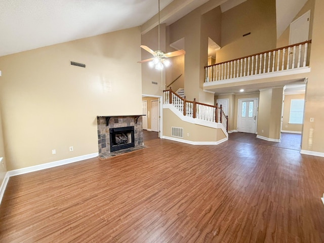 unfurnished living room featuring wood-type flooring, high vaulted ceiling, ceiling fan, and a stone fireplace