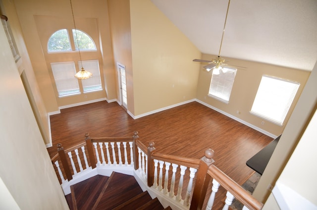 staircase with high vaulted ceiling, wood-type flooring, and ceiling fan with notable chandelier