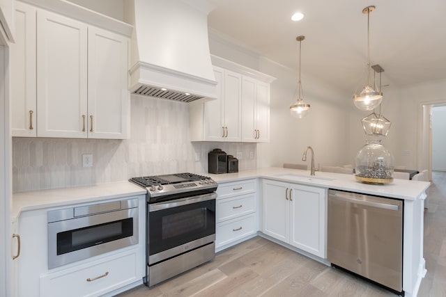 kitchen with custom exhaust hood, light wood-type flooring, appliances with stainless steel finishes, decorative light fixtures, and white cabinetry