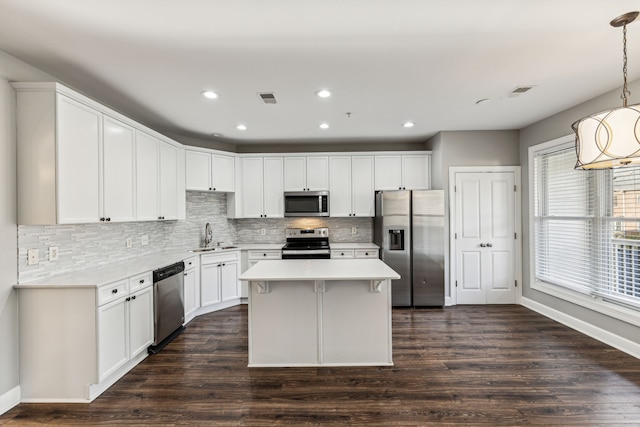 kitchen with appliances with stainless steel finishes, a center island, dark wood-type flooring, and pendant lighting