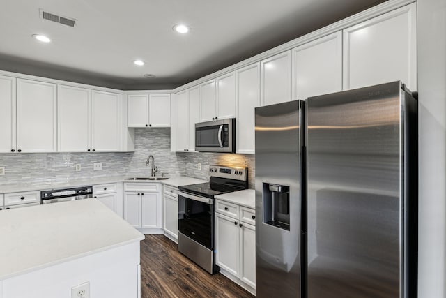 kitchen with appliances with stainless steel finishes, backsplash, dark wood-type flooring, sink, and white cabinets