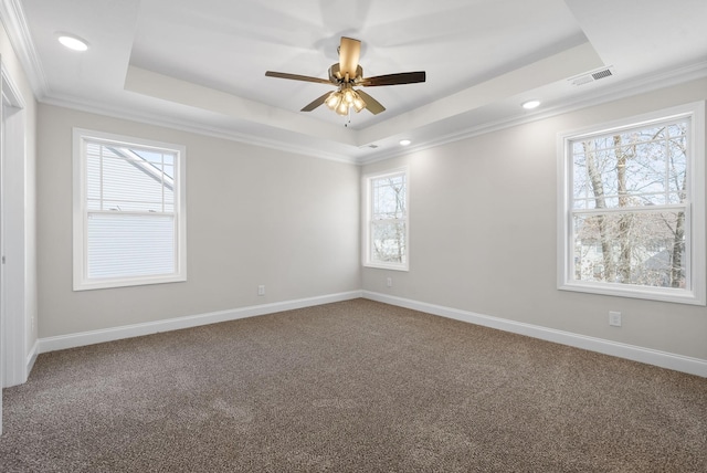 carpeted spare room with ornamental molding, a tray ceiling, visible vents, and baseboards