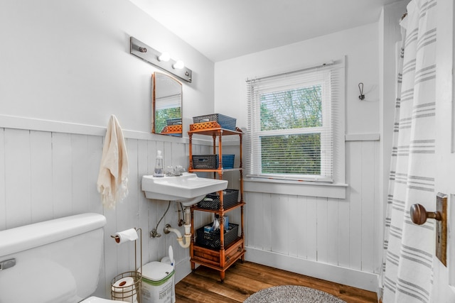 bathroom with sink, a shower with curtain, wood walls, wood-type flooring, and toilet