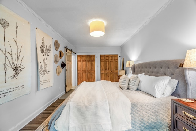 bedroom with a barn door, dark hardwood / wood-style flooring, crown molding, and two closets