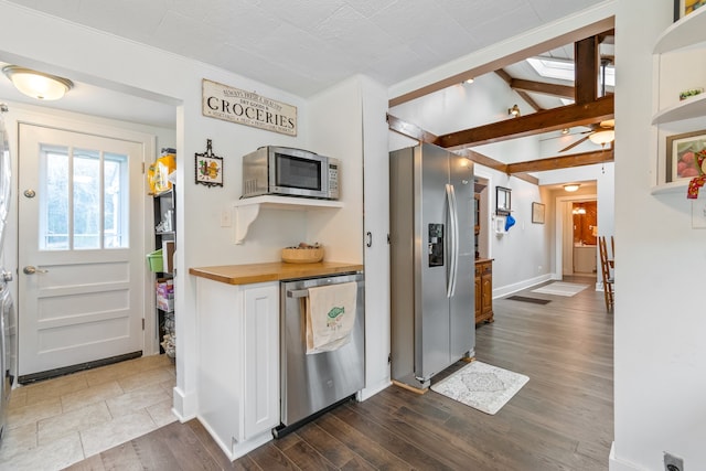 kitchen featuring dark wood-type flooring, wooden counters, white cabinets, vaulted ceiling with skylight, and stainless steel appliances