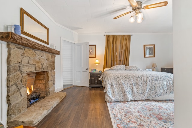 bedroom featuring ceiling fan, a stone fireplace, dark wood-type flooring, and crown molding