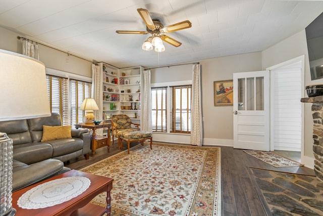 living room with dark hardwood / wood-style floors, a healthy amount of sunlight, a stone fireplace, and ceiling fan