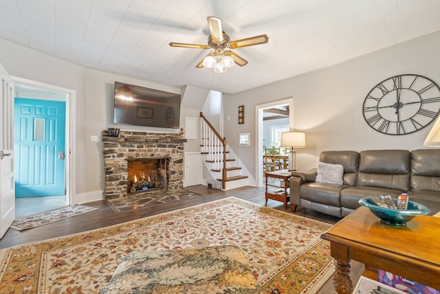 living room featuring ceiling fan, a stone fireplace, and dark hardwood / wood-style flooring