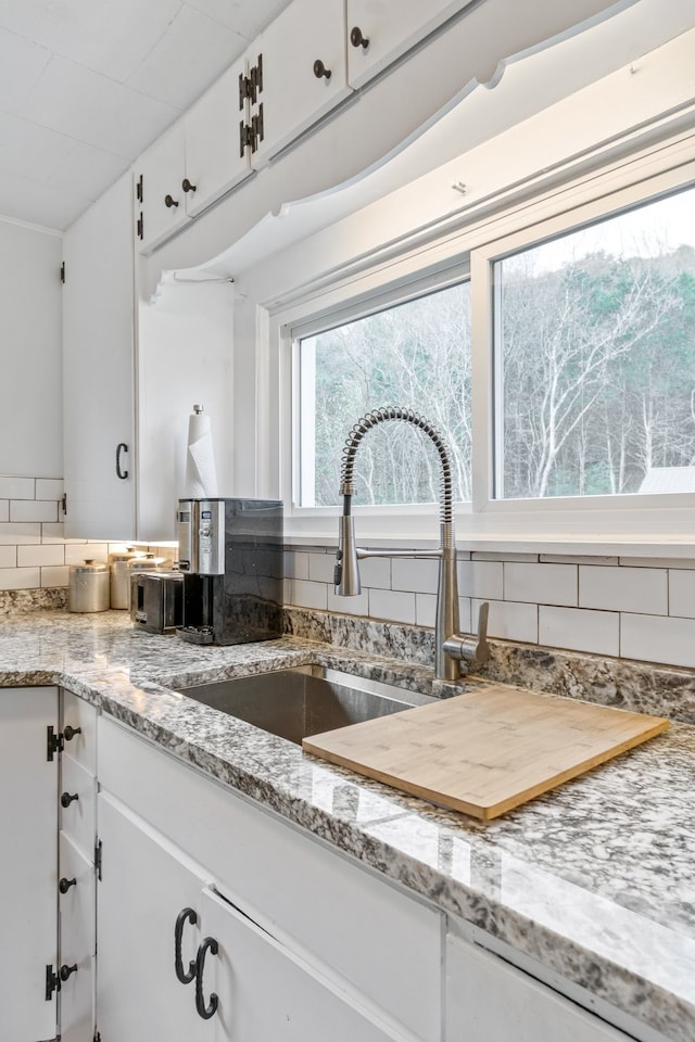 interior space with decorative backsplash, sink, white cabinets, and light stone countertops