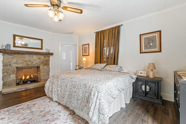 bedroom with crown molding, ceiling fan, dark wood-type flooring, and a stone fireplace