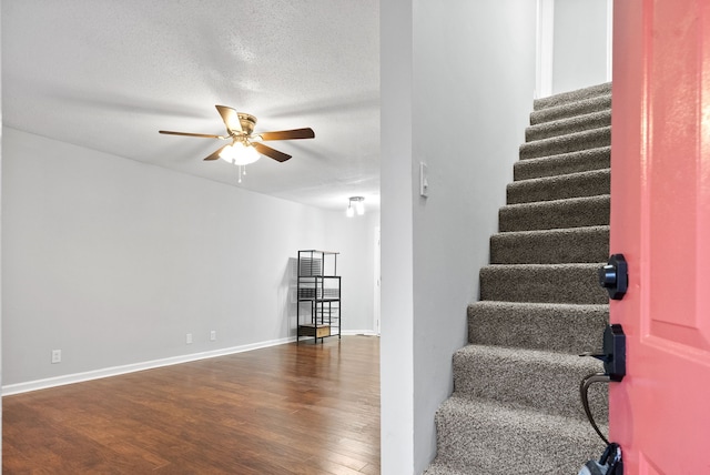 stairway featuring ceiling fan, wood-type flooring, and a textured ceiling