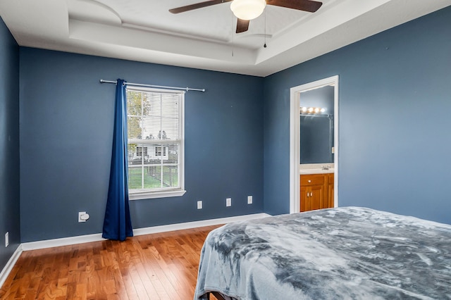 bedroom with hardwood / wood-style flooring, ceiling fan, a raised ceiling, and connected bathroom