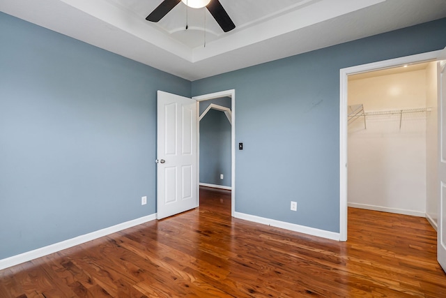 unfurnished bedroom with a spacious closet, ceiling fan, wood-type flooring, and a closet