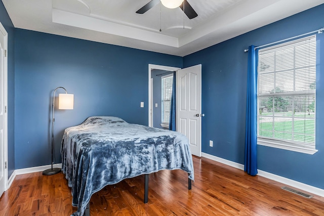 bedroom with hardwood / wood-style floors, a tray ceiling, and ceiling fan