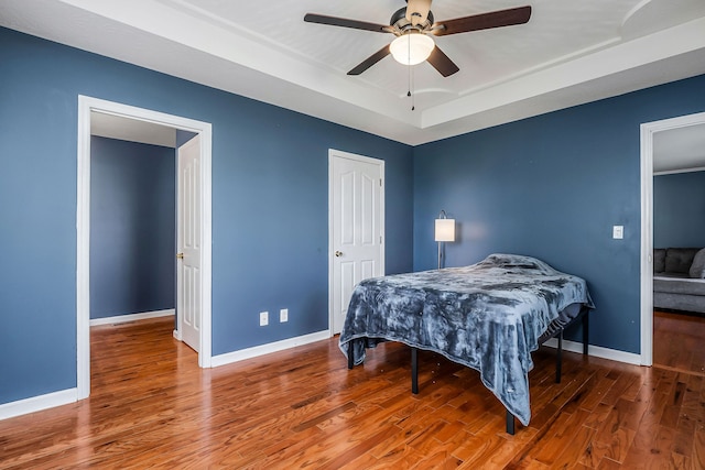 bedroom with hardwood / wood-style flooring, a raised ceiling, and ceiling fan