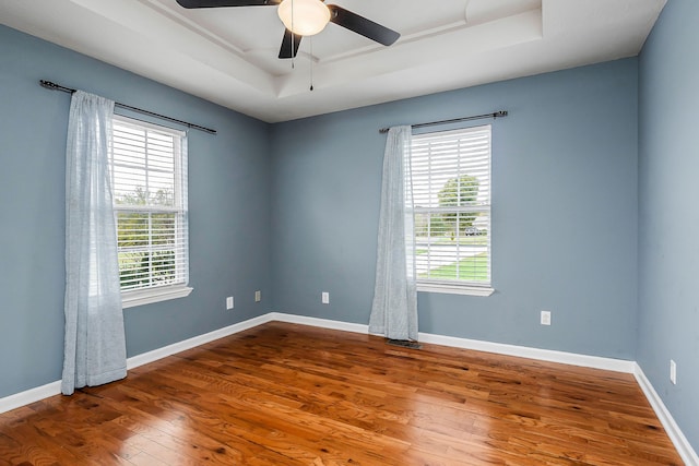 unfurnished room with wood-type flooring, a raised ceiling, plenty of natural light, and ceiling fan