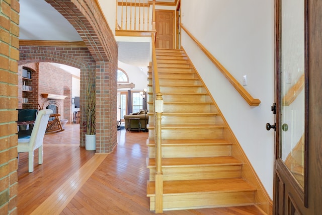 staircase with a high ceiling, a fireplace, wood-type flooring, and brick wall