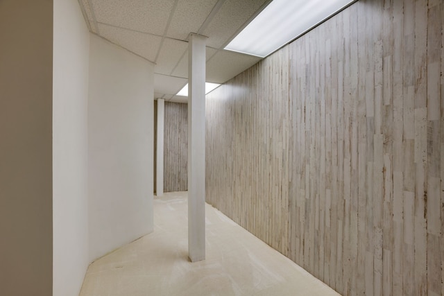 basement featuring a paneled ceiling, wood walls, and light carpet