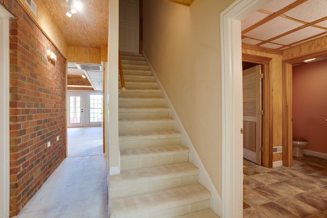 stairs with carpet flooring, brick wall, and french doors