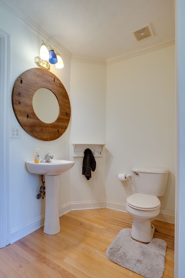 bathroom with hardwood / wood-style floors, toilet, ornamental molding, and a textured ceiling