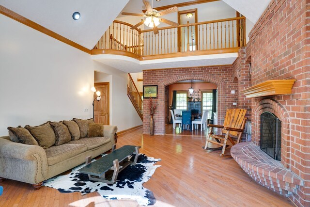 living room featuring ceiling fan, light wood-type flooring, ornamental molding, and a towering ceiling