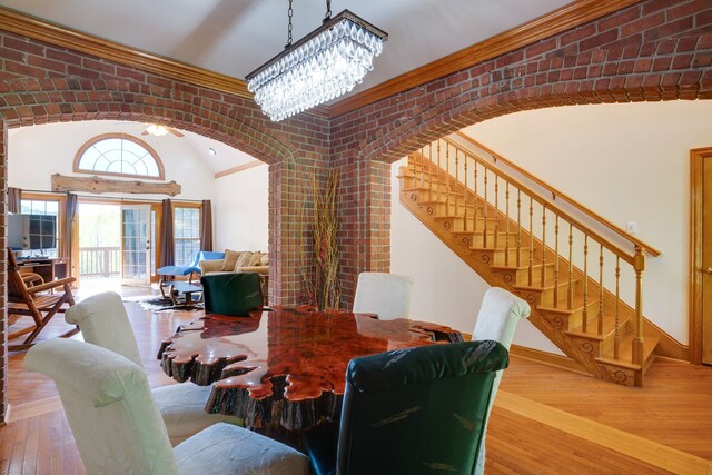 dining area featuring hardwood / wood-style floors, brick wall, vaulted ceiling, and a notable chandelier