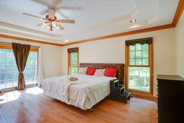 bedroom with light wood-type flooring, ornamental molding, access to outside, a tray ceiling, and ceiling fan