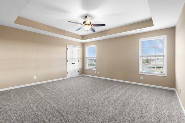 carpeted empty room with a raised ceiling and ceiling fan