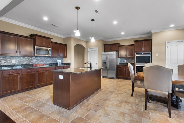 kitchen with a kitchen island with sink, hanging light fixtures, dark stone countertops, ornamental molding, and stainless steel appliances