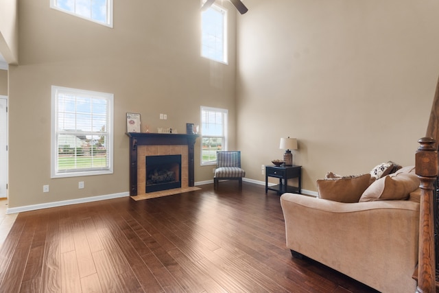 living room with ceiling fan, a tile fireplace, dark wood-type flooring, and a high ceiling