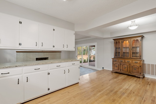 kitchen with white cabinetry, tasteful backsplash, light stone counters, a textured ceiling, and light wood-type flooring