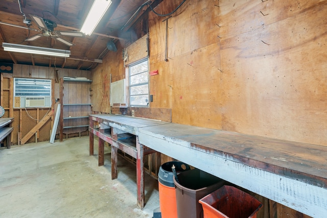 basement with a workshop area, ceiling fan, cooling unit, and wood walls