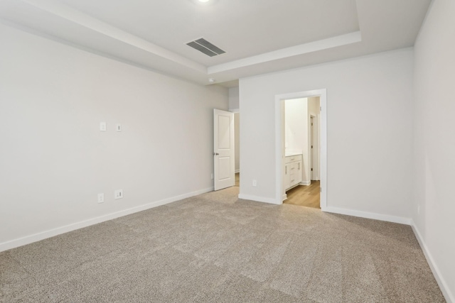 unfurnished bedroom with connected bathroom, light colored carpet, and a raised ceiling