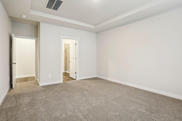 unfurnished bedroom featuring light carpet, connected bathroom, and a raised ceiling